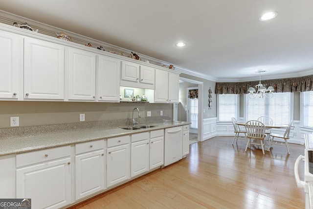 kitchen with a sink, an inviting chandelier, white cabinetry, white dishwasher, and ornamental molding