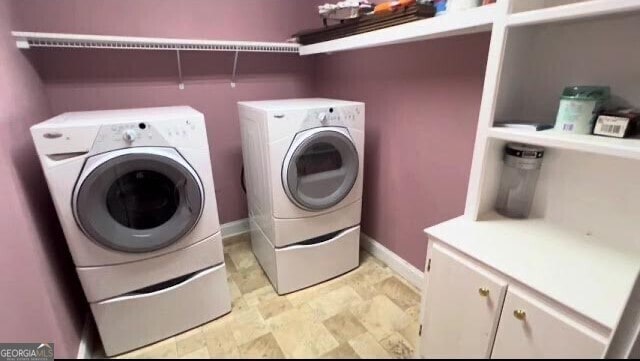 laundry room featuring washing machine and clothes dryer, baseboards, and cabinet space