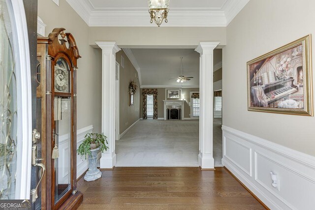 corridor featuring decorative columns, wood finished floors, a wainscoted wall, and ornamental molding