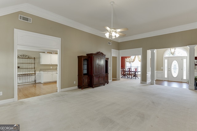 carpeted foyer featuring ceiling fan with notable chandelier, ornate columns, and crown molding