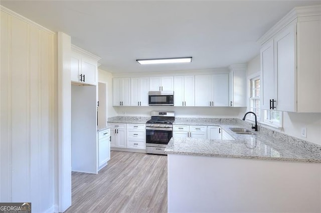 kitchen featuring kitchen peninsula, white cabinets, appliances with stainless steel finishes, light hardwood / wood-style floors, and sink