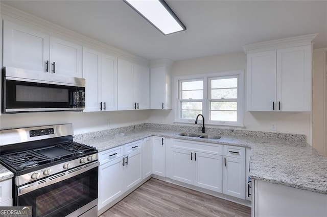 kitchen featuring appliances with stainless steel finishes, white cabinetry, light stone countertops, light hardwood / wood-style flooring, and sink