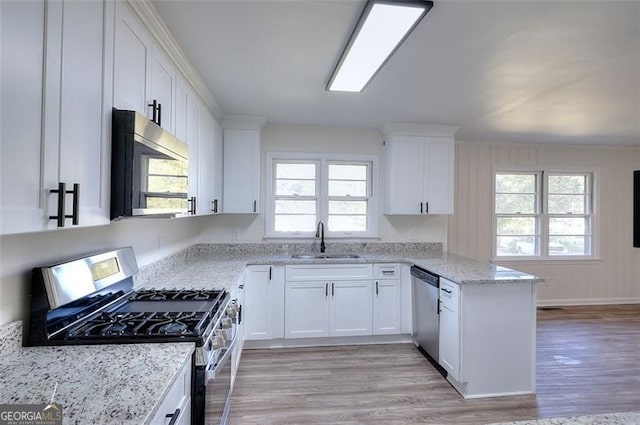 kitchen featuring appliances with stainless steel finishes, sink, light wood-type flooring, white cabinetry, and a wealth of natural light