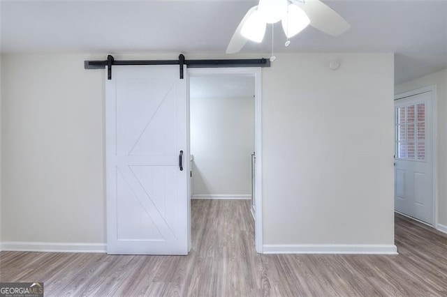 unfurnished bedroom with ceiling fan, light wood-type flooring, and a barn door