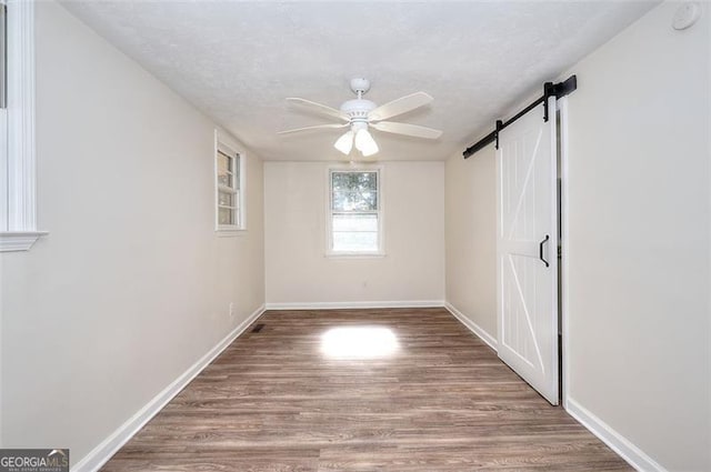 empty room with a textured ceiling, a barn door, hardwood / wood-style flooring, and ceiling fan