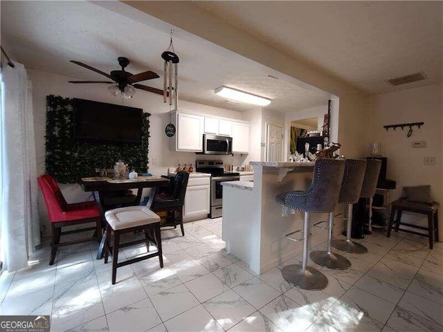 kitchen with a breakfast bar area, kitchen peninsula, stainless steel appliances, white cabinets, and ceiling fan