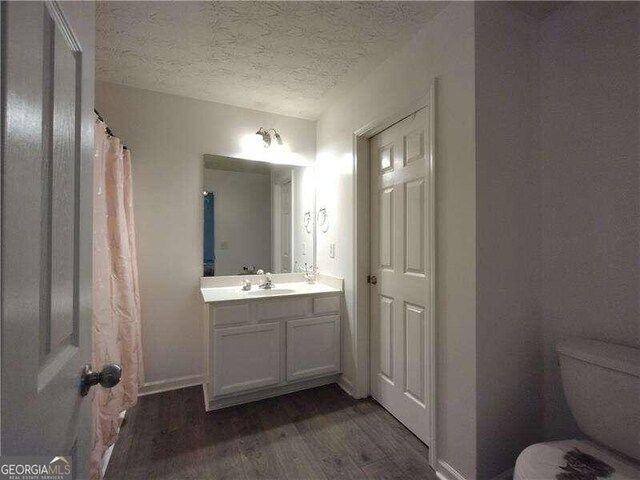 bathroom featuring a textured ceiling, wood-type flooring, toilet, vanity, and curtained shower