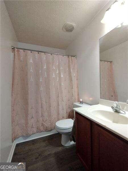 bathroom featuring a textured ceiling, wood-type flooring, toilet, vanity, and a shower with shower curtain