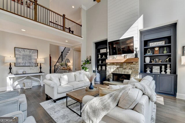 living room with a stone fireplace, ornamental molding, a high ceiling, and dark hardwood / wood-style floors