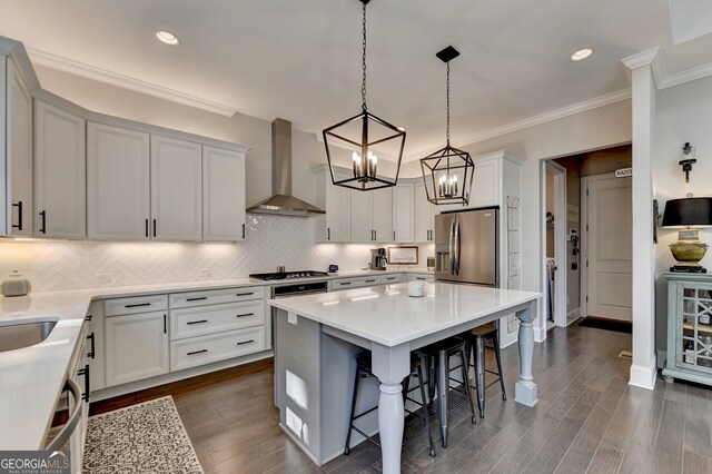 kitchen featuring dark hardwood / wood-style floors, wall chimney exhaust hood, a kitchen breakfast bar, stainless steel appliances, and pendant lighting