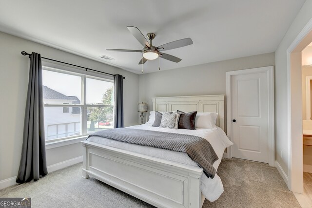 bedroom with ceiling fan, light carpet, and ensuite bathroom