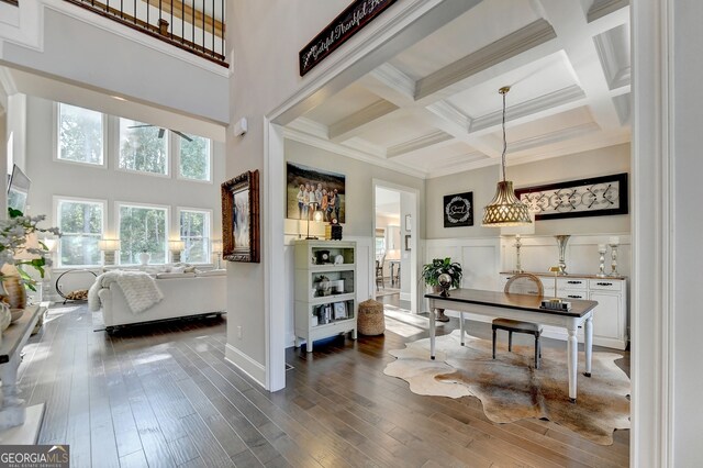 interior space with a towering ceiling, coffered ceiling, beamed ceiling, ornamental molding, and dark hardwood / wood-style floors