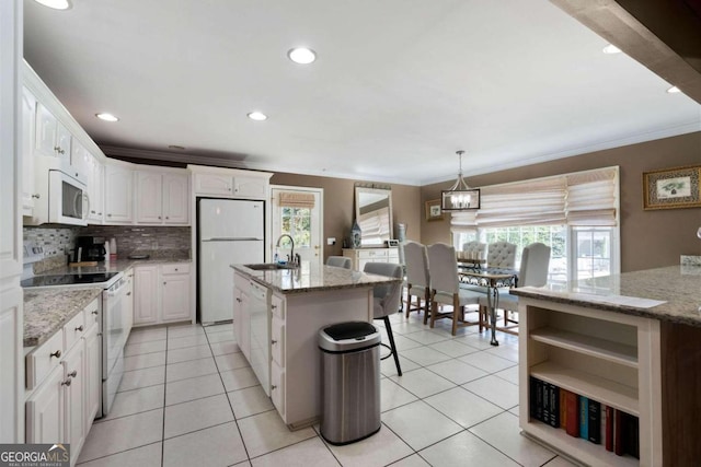 kitchen featuring an island with sink, white cabinets, plenty of natural light, and white appliances