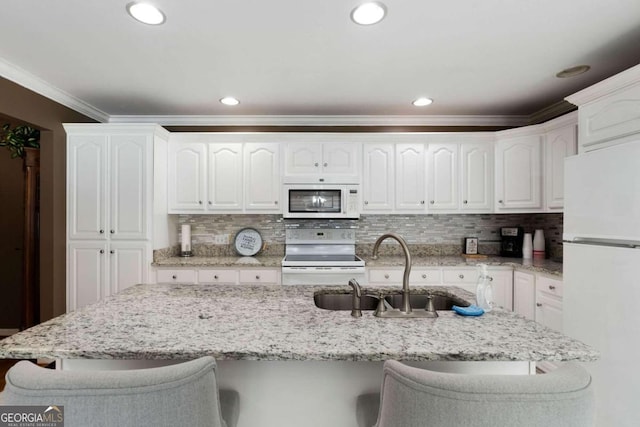 kitchen with decorative backsplash, white cabinets, a kitchen breakfast bar, sink, and white appliances