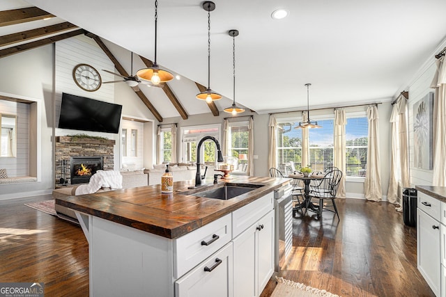 kitchen with sink, a fireplace, wood counters, pendant lighting, and a center island with sink