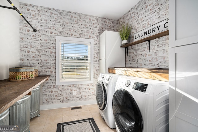 clothes washing area with brick wall, washer and clothes dryer, and light tile patterned floors