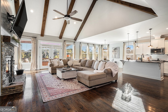 living room with a stone fireplace, dark hardwood / wood-style floors, beam ceiling, high vaulted ceiling, and ceiling fan