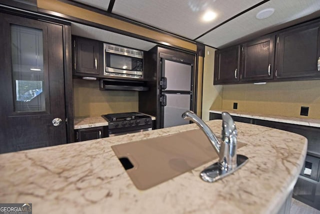 kitchen featuring sink, built in appliances, light stone counters, and backsplash