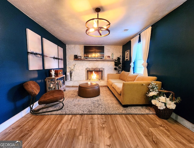 living room featuring a stone fireplace, a chandelier, and wood-type flooring