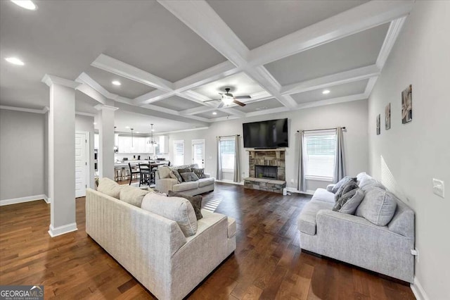 living room with a stone fireplace, ceiling fan, beamed ceiling, and dark hardwood / wood-style flooring