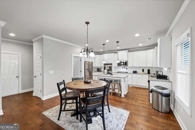 dining room featuring sink, crown molding, a notable chandelier, and dark hardwood / wood-style flooring