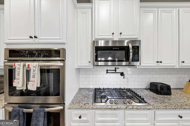 kitchen featuring white cabinetry, light stone counters, stainless steel appliances, and decorative backsplash