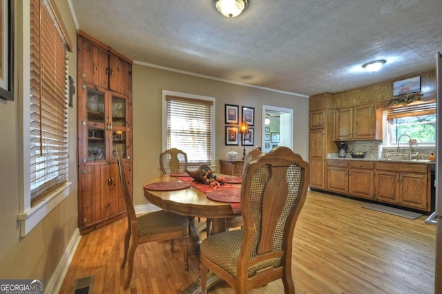 dining space featuring light hardwood / wood-style floors, ornamental molding, sink, and plenty of natural light