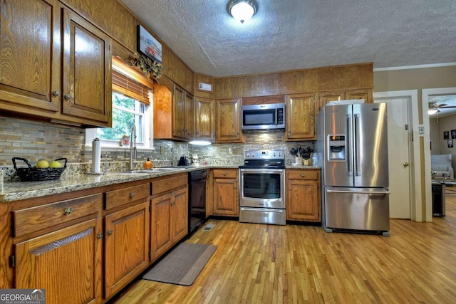 kitchen with decorative backsplash, appliances with stainless steel finishes, light hardwood / wood-style flooring, sink, and light stone counters