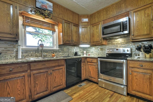 kitchen featuring stainless steel appliances, sink, light stone countertops, light wood-type flooring, and a textured ceiling