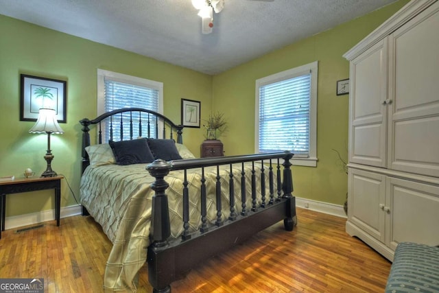 bedroom with hardwood / wood-style floors, multiple windows, a textured ceiling, and ceiling fan