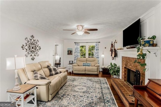 living room with wood-type flooring, a textured ceiling, a brick fireplace, and ceiling fan