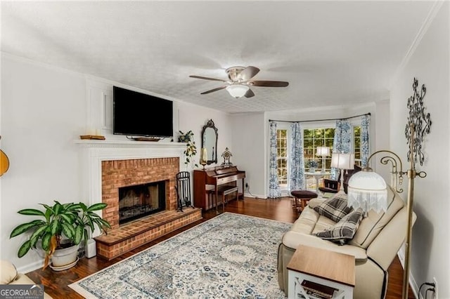 living room with ornamental molding, a brick fireplace, ceiling fan, and dark wood-type flooring