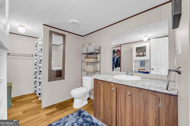 bathroom with a textured ceiling, hardwood / wood-style flooring, toilet, vanity, and crown molding