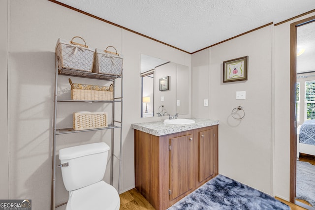 bathroom featuring wood-type flooring, a textured ceiling, toilet, vanity, and crown molding