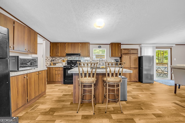 kitchen with light hardwood / wood-style floors, black appliances, a kitchen island, and a wealth of natural light