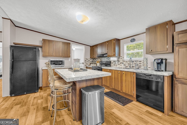 kitchen with a kitchen island, a textured ceiling, light hardwood / wood-style flooring, black appliances, and sink