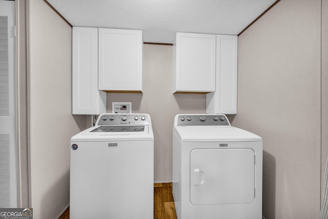 clothes washing area with cabinets, a textured ceiling, hardwood / wood-style floors, and separate washer and dryer