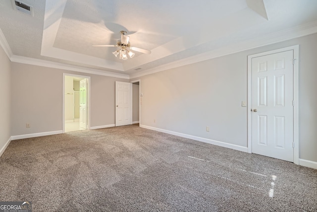 unfurnished bedroom featuring a tray ceiling, ensuite bath, ornamental molding, carpet flooring, and ceiling fan