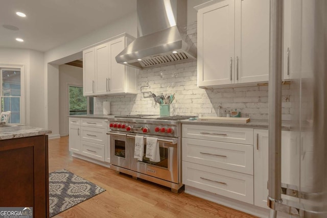 kitchen featuring light hardwood / wood-style floors, wall chimney exhaust hood, white cabinetry, and range with two ovens