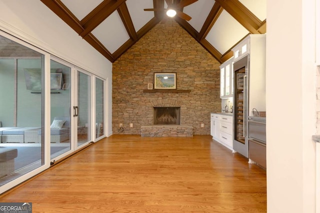 unfurnished living room with a stone fireplace, beam ceiling, light wood-type flooring, high vaulted ceiling, and ceiling fan