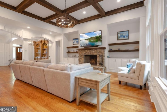 living room featuring a stone fireplace, light hardwood / wood-style flooring, beam ceiling, and coffered ceiling