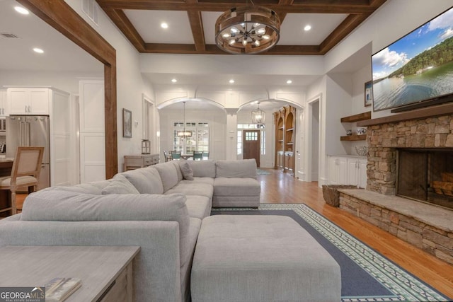 living room with a stone fireplace, hardwood / wood-style floors, coffered ceiling, beamed ceiling, and a notable chandelier