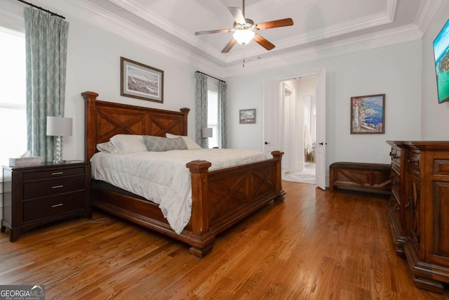 bedroom with wood-type flooring, crown molding, a raised ceiling, ensuite bathroom, and ceiling fan