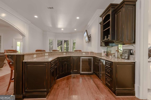 kitchen featuring kitchen peninsula, wine cooler, a breakfast bar area, light wood-type flooring, and dark brown cabinetry