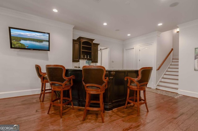 bar with light hardwood / wood-style floors, crown molding, and dark brown cabinets