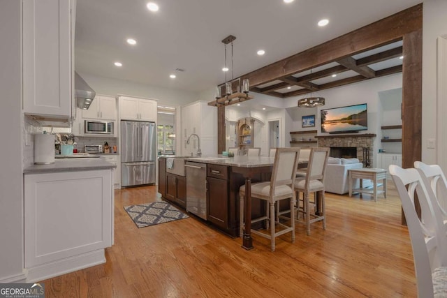 kitchen with appliances with stainless steel finishes, white cabinetry, light hardwood / wood-style floors, pendant lighting, and a center island with sink