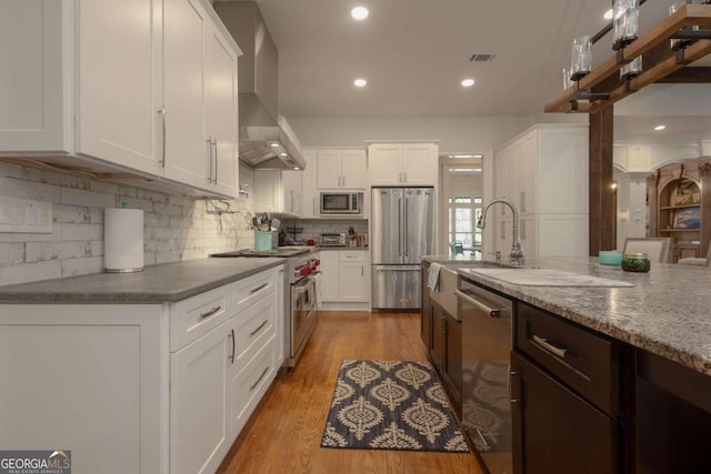 kitchen with light hardwood / wood-style floors, stainless steel appliances, wall chimney range hood, and white cabinets