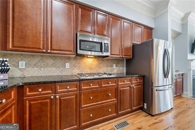 kitchen with dark stone countertops, crown molding, appliances with stainless steel finishes, and decorative backsplash