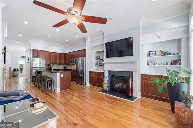 living room with sink, crown molding, built in shelves, light hardwood / wood-style floors, and ceiling fan