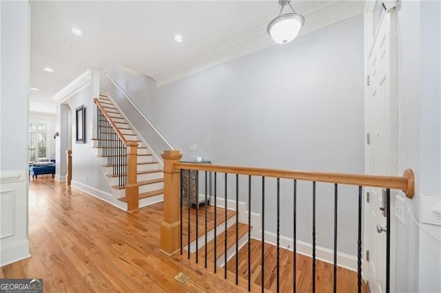 stairs with ornamental molding and hardwood / wood-style floors